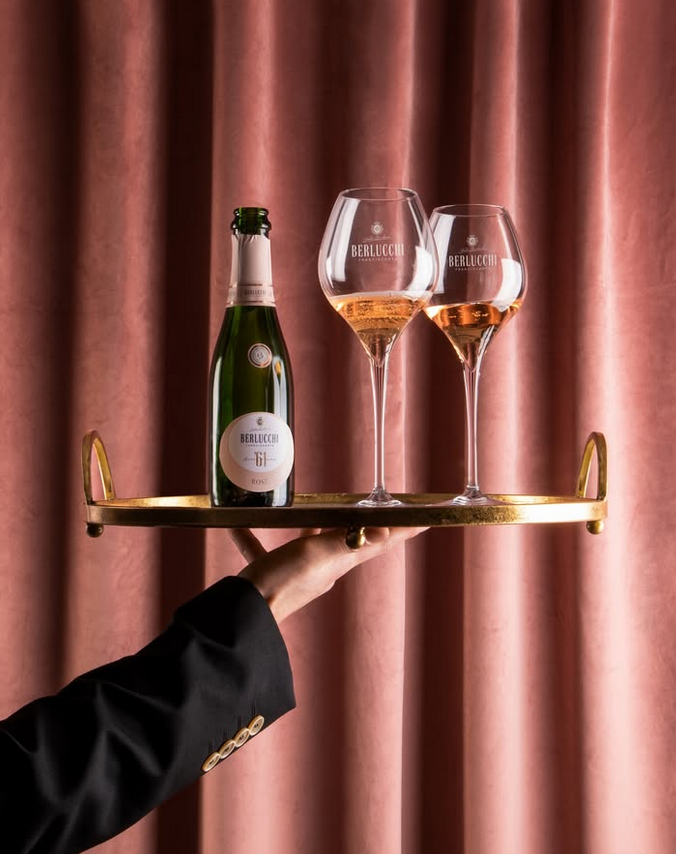 hochgehaltenes Tablett mit Berlucchi 61 Franciacorta Rosé 2 Gläsern