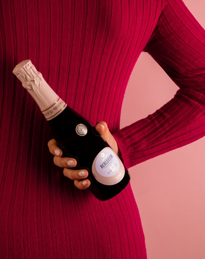 Frau im roten Kleid hält eine Flasche Berlucchi 61 Franciacorta Rosé hinter ihren Rücken