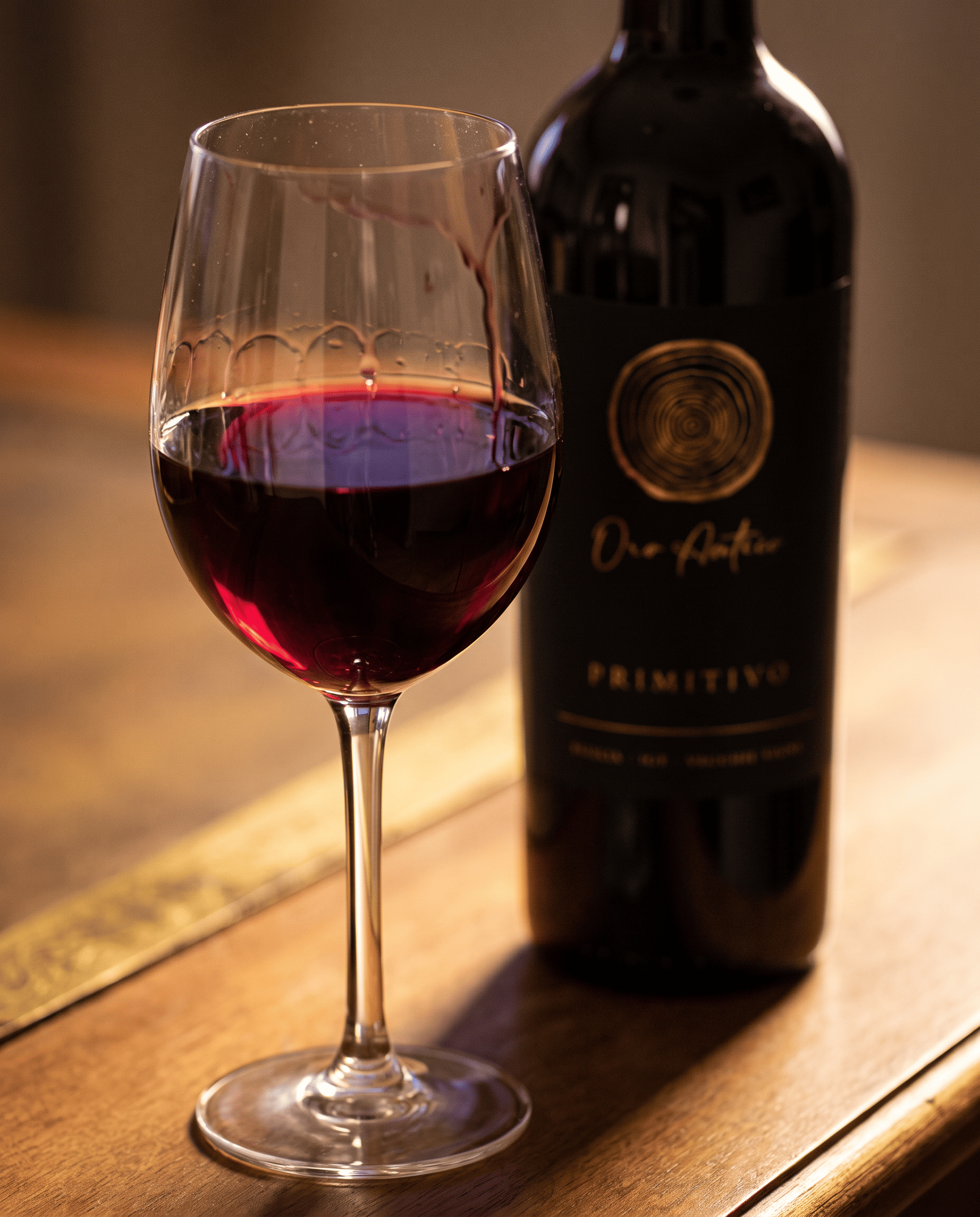 Ein Glas Oro Antico Primitivo, tiefes Rubinrot im warmen Gegenlicht