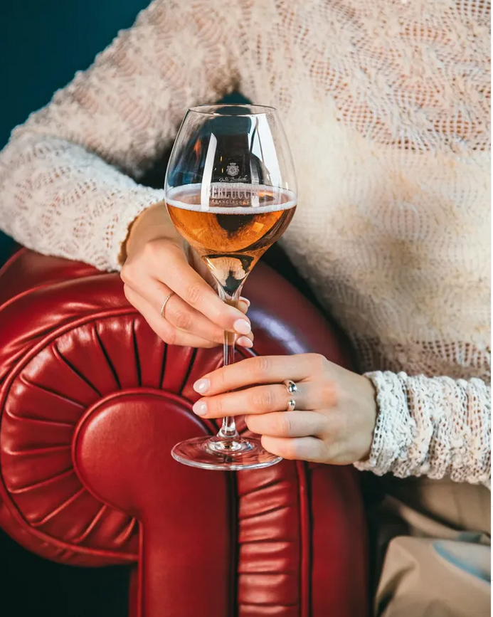 Frau sitzt auf roter Ledercouch mit Berlucchi Glas in der Hand